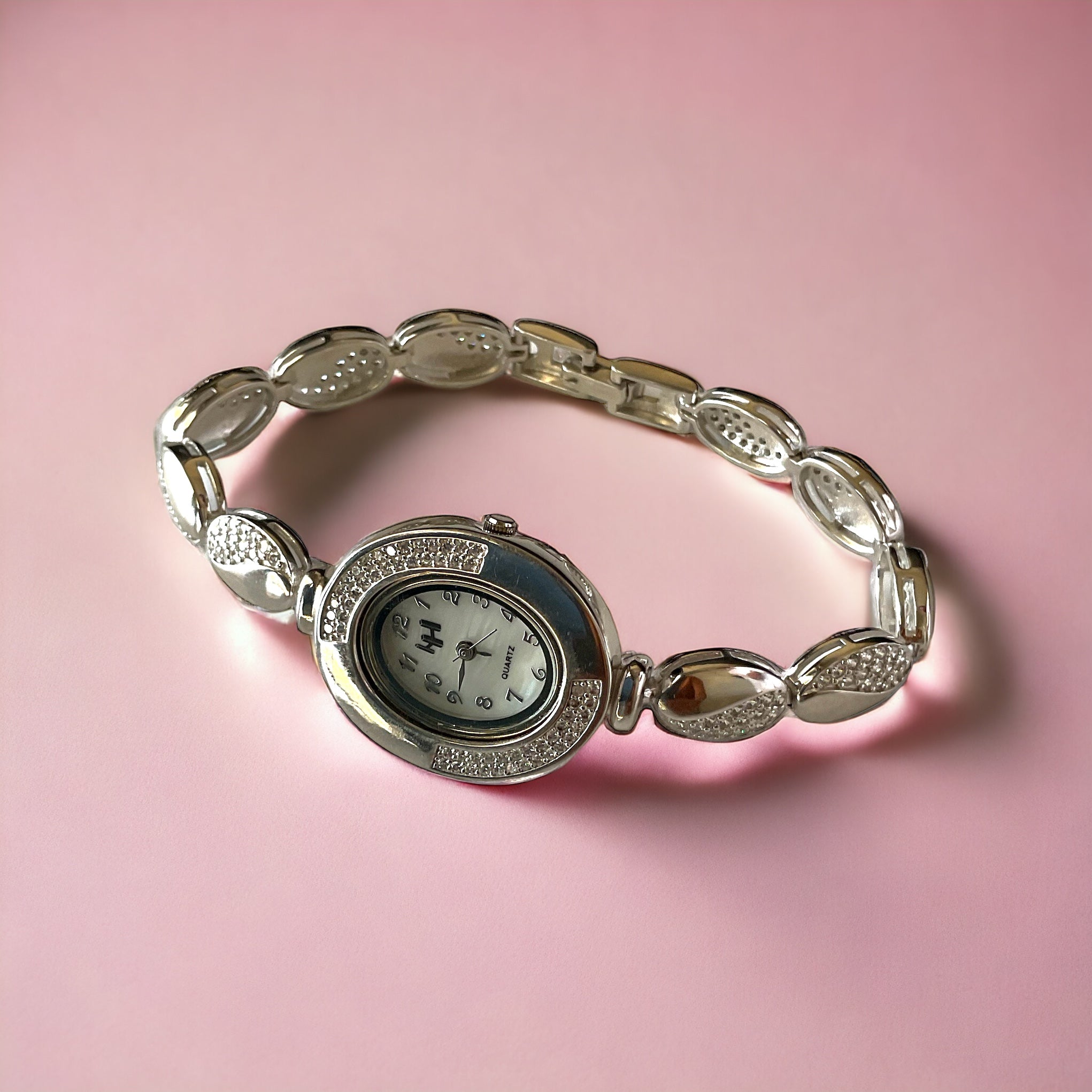 a silver watch sitting on top of a pink surface