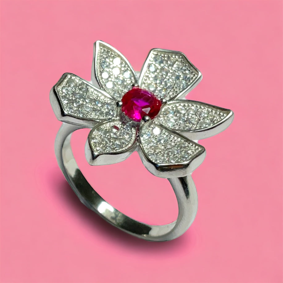a silver ring with a flower and a red stone