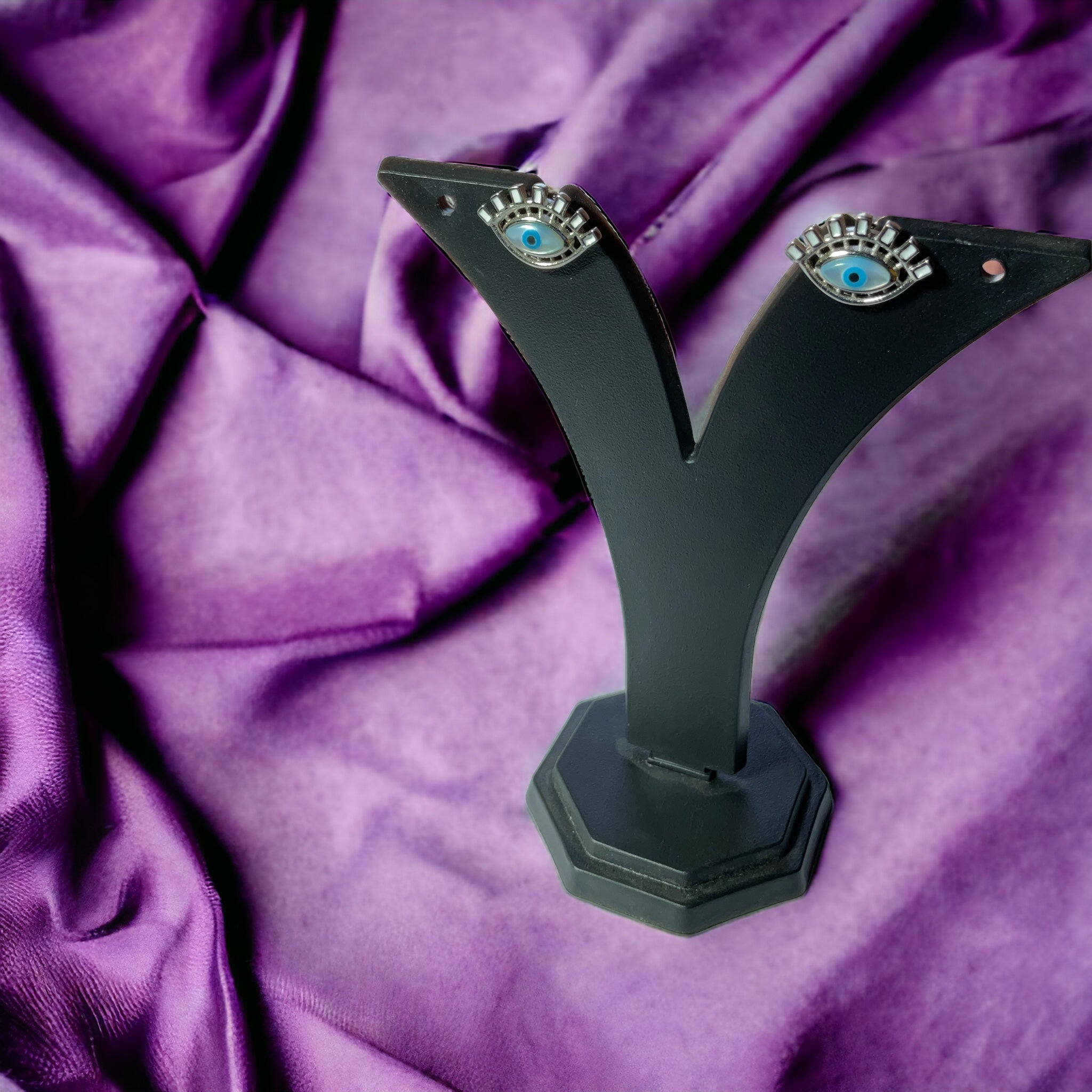 a pair of black earrings with blue eyes on a purple cloth