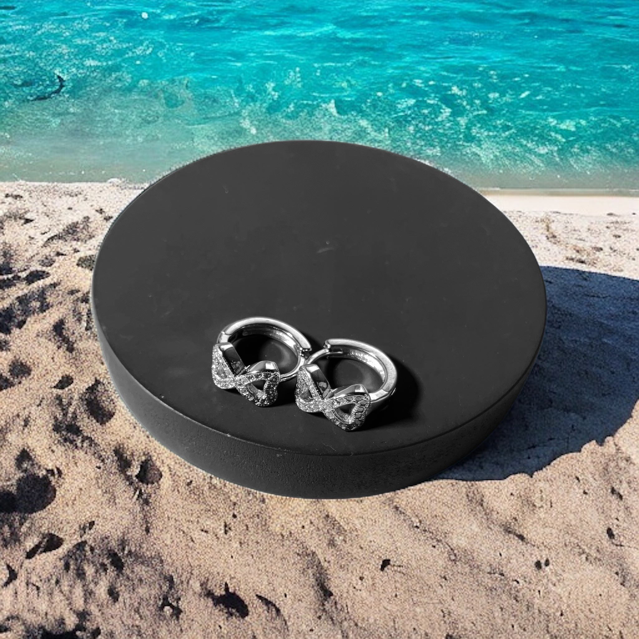 a pair of silver wedding rings sitting on a black round box on a sandy beach