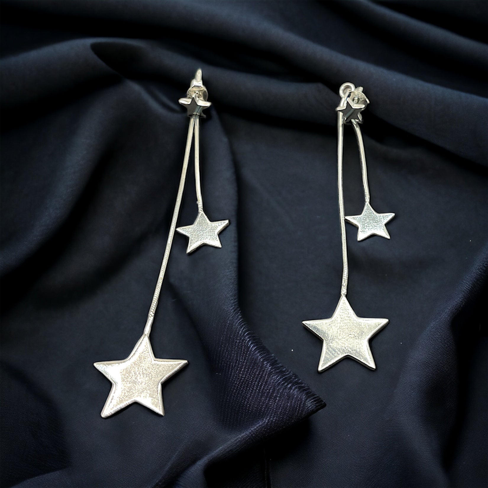 a pair of silver stars hanging from a black cloth