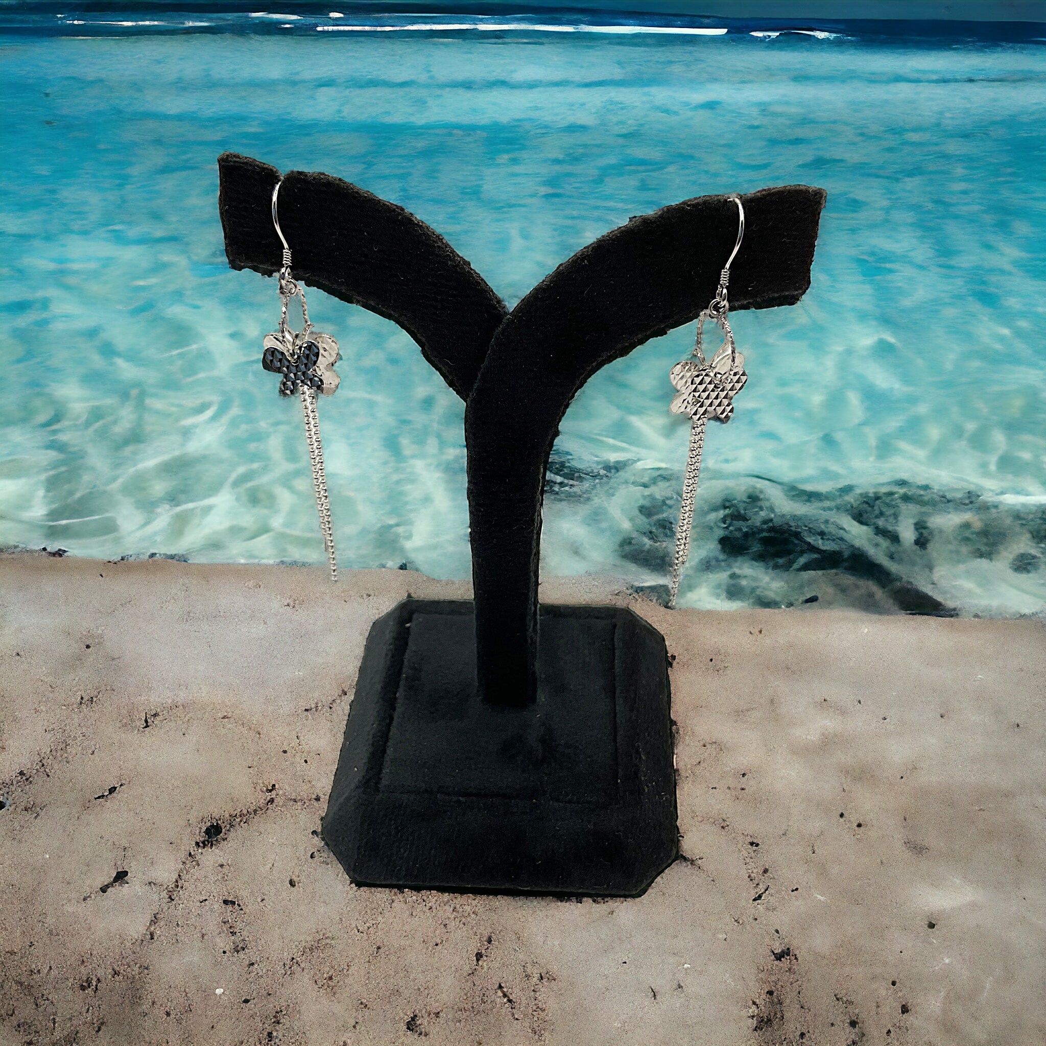 a pair of earrings are on a stand in front of a body of water