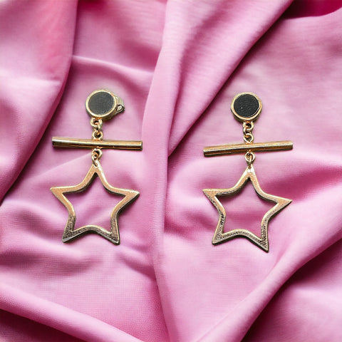 a pair of star shaped earrings on a pink cloth