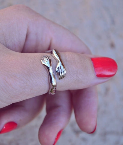 a woman's hand holding a gold ring with two forks on it