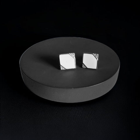 a pair of square shaped earrings sitting on a black plate