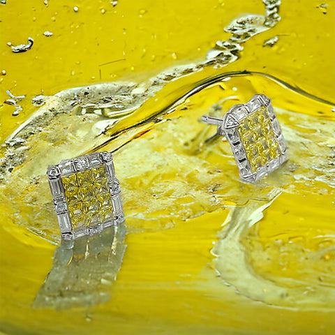 a pair of yellow diamond earrings sitting on top of a yellow liquid