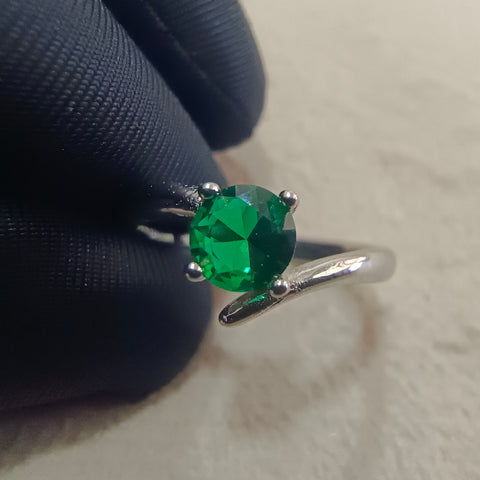 a close up of a person's hand holding a ring with a green stone